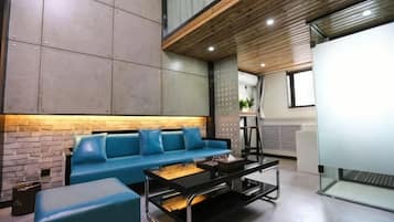 Un área de estar moderna con un sofá azul, un separador de vidrio y un techo de madera.
