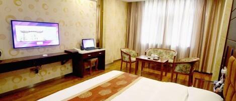 A hotel room with a bed, a desk with a laptop, a television, and a seating area with chairs.
