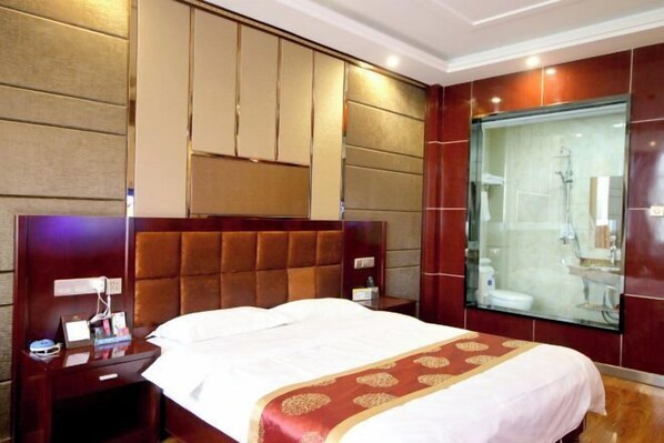 Ein Hotelzimmer mit einem großen Bett, einem Nachttisch, einer Duschkabine und einem wandmontierten Waschtisch.