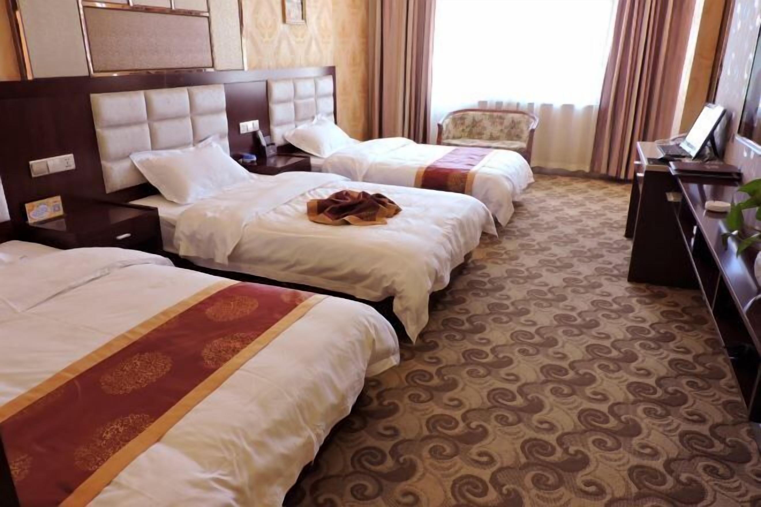 A hotel room with two beds, a desk, a chair, and a patterned carpet.