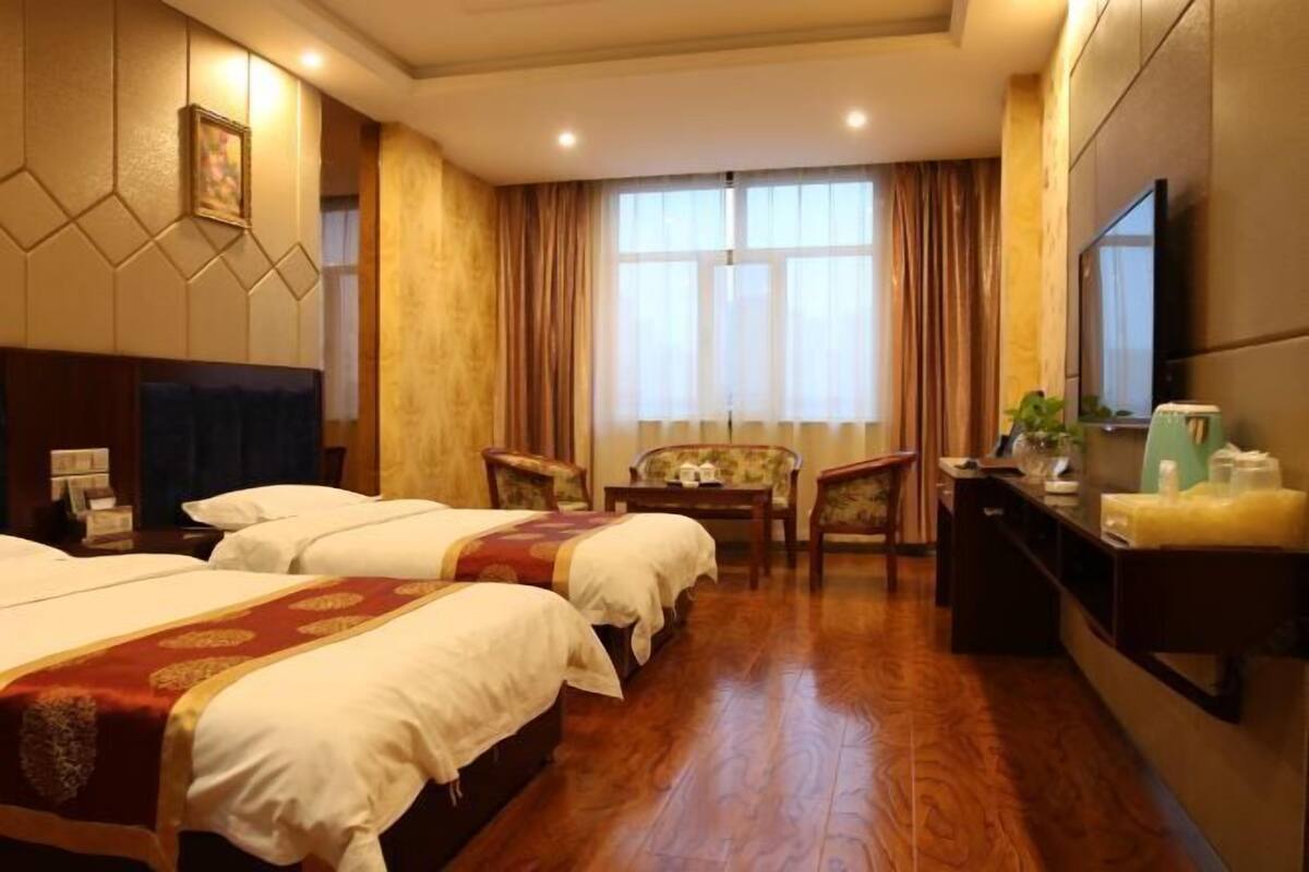 Habitación de hotel con dos camas, un escritorio, una silla, un televisor y una ventana con cortinas.