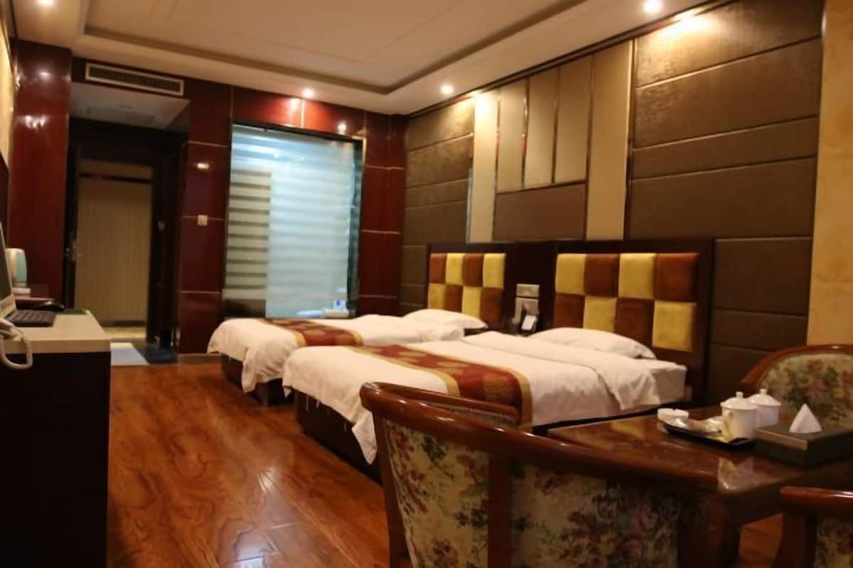 Habitación de hotel con dos camas, un escritorio, una silla y una ventana con persianas.