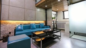 A modern lounge area with a blue sofa, a black coffee table, and a brick accent wall. - Feitian Hotel (Jingyuan)