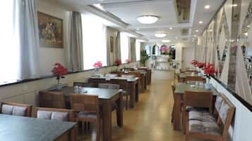 A restaurant with multiple tables and chairs, a long counter, and a view of the kitchen area.