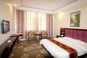 A hotel room with a large bed, a desk, two chairs, a small table, and a painting on the wall. - Feitian Hotel (Jingyuan)