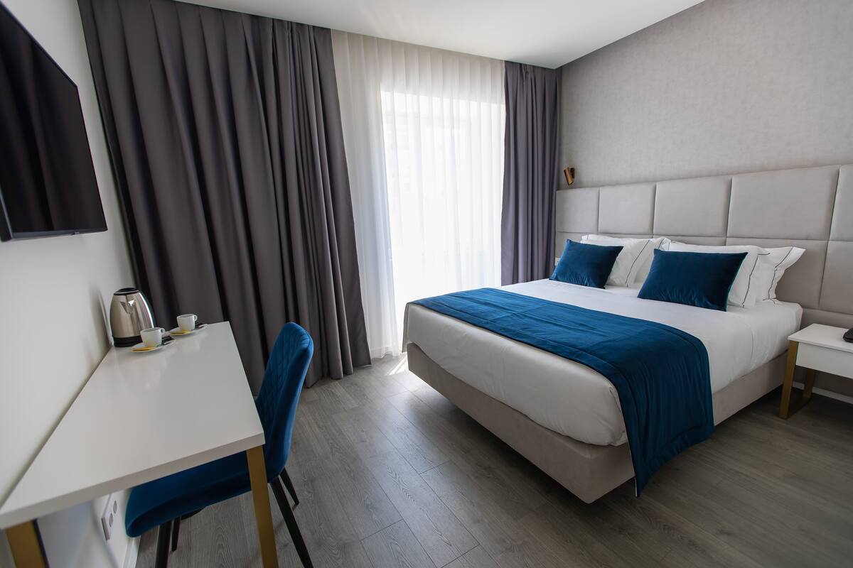 A hotel room with a bed, a desk, a chair, a coffee maker, and curtains.