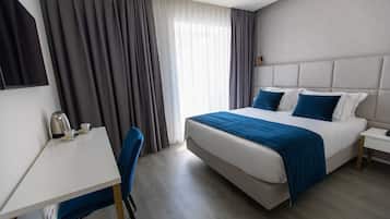 Una habitación de hotel con cama, escritorio, silla, cafetera y cortinas.