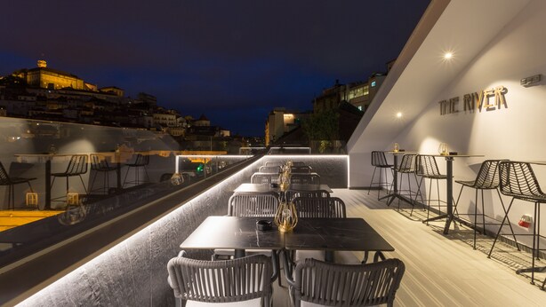 A rooftop dining area with tables and chairs, overlooking a cityscape at night. - Hotel Mondego (Coimbra)
