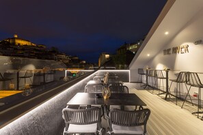 A rooftop dining area with tables and chairs, overlooking a cityscape at night. - Hotel Mondego (Coimbra)