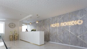 A modern hotel reception with a clean, minimalist design, featuring a reception desk, a clock, and a neon sign that reads "HOTEL MONDEGO". - Hotel Mondego (Coimbra)