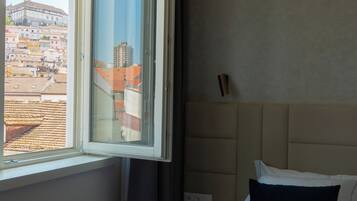 A hotel room with a bed, a nightstand, a window with a view of buildings, and a headboard.