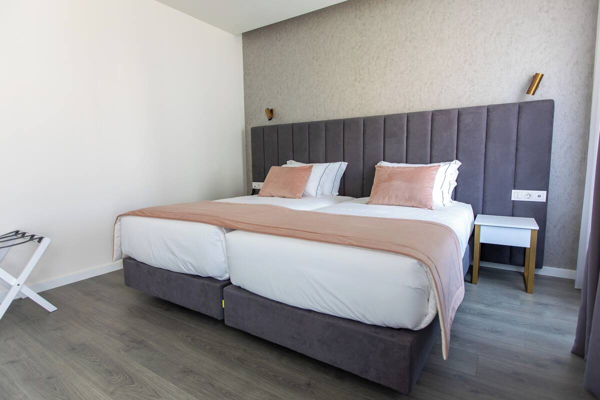 A modern bedroom with a large bed, grey headboard, and a small bedside table.