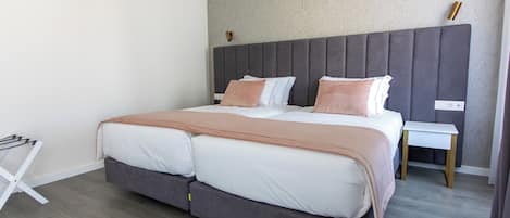 A modern bedroom with a large bed, grey headboard, and a small bedside table.
