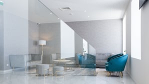 A modern interior with a sofa, ottoman, and chairs, a staircase, and a large window. - Hotel Mondego (Coimbra)
