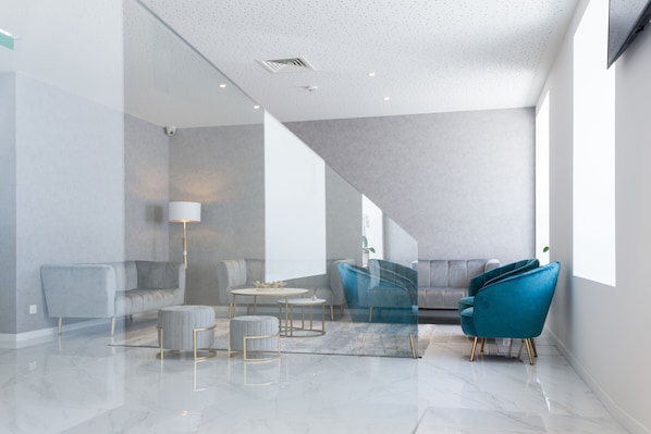 A modern interior with a sofa, ottoman, and chairs, a staircase, and a large window. - Hotel Mondego (Coimbra)