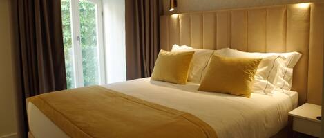 A large bed with a headboard, a bedside table, and a window with curtains.