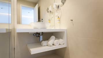 A modern bathroom with a white sink, a mirror, and a shelf with rolled towels.