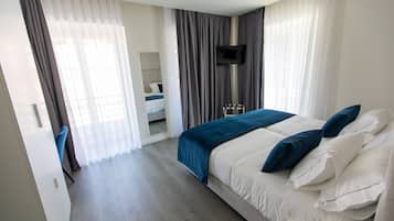 Ein modernes Hotelzimmer mit einem großen Bett, einem an der Wand montierten Fernseher und einem durch eine Glastür einsehbarer Badezimmer.