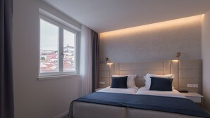 A modern hotel room with a large bed, bedside tables, and a view of the city through a large window. - Hotel Mondego (Coimbra)