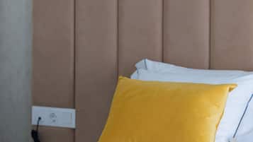 A bed with a beige headboard, white bedding, and a yellow accent pillow.