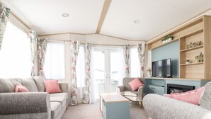 A modern living room with a grey sofa, a small table, and a TV on a wooden shelf. - 109 Bude (Truro)