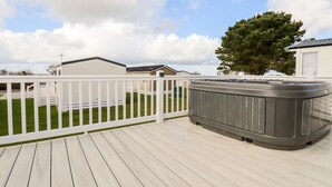 A deck with a hot tub, white railings, and a grassy yard with a tree. - 109 Bude (Truro)