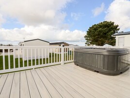 Una terraza con jacuzzi, barandillas blancas y un patio cubierto de césped con un árbol.