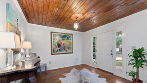 Una habitación con techo de madera, una puerta blanca, un cuadro, un escritorio con lámpara y un tapiz de cuero de vaca.