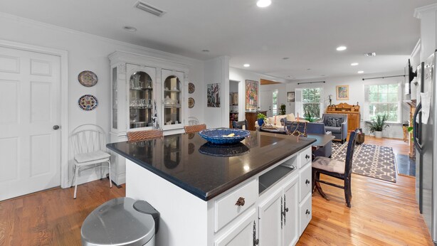 Una cocina amplia con una isla central, muebles blancos y un comedor con un tapete estampado.