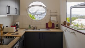 Moderni keittiö, jossa on pyöreä ikkuna, integroidut kodinkoneet ja näkymä vehreään maisemaan.