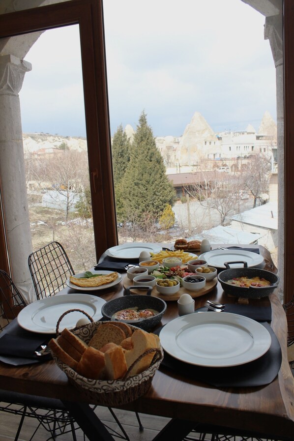 A breakfast table with various dishes and bread, set against a view of a mountainous landscape. - Kayra Cave Suites (Nevsehir)