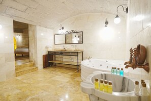 A modern bathroom with a marble floor, a freestanding bathtub, a vanity with a mirror, and a wooden fish sculpture. - Kayra Cave Suites (Nevsehir)