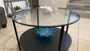 Une table ronde en verre avec un pied noir, un bol en verre bleu et un objet décoratif blanc posé sur le dessus.