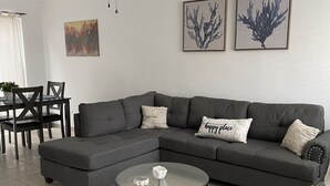 Un salon moderne avec un canapé d’angle, une table basse en verre et un ventilateur de plafond.