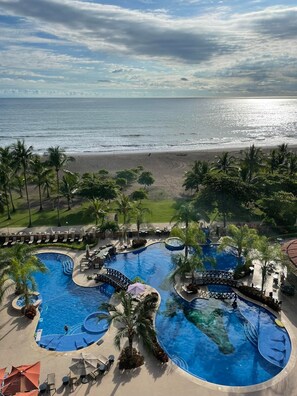 A resort with a large pool area, palm trees, and a beach view. - Beach Front Condo , located in 5* Crocs Hotel (Jacó)