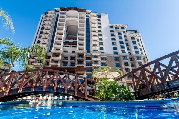 A high-rise hotel with multiple balconies, a swimming pool, and a bridge. - Beach Front Condo , located in 5* Crocs Hotel (Jacó)