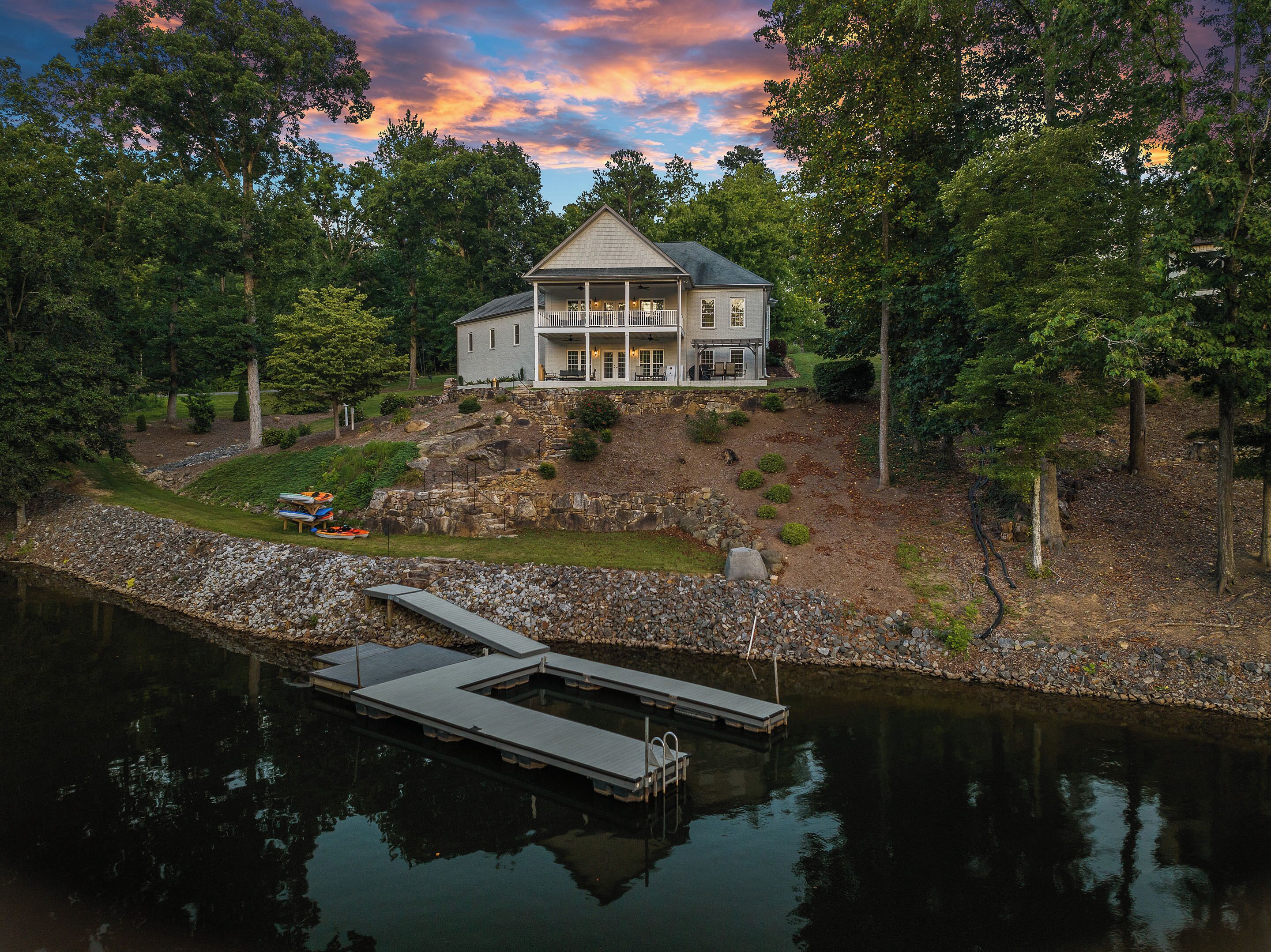 A large house with a porch, a dock extending into a lake, and a rocky hillside.