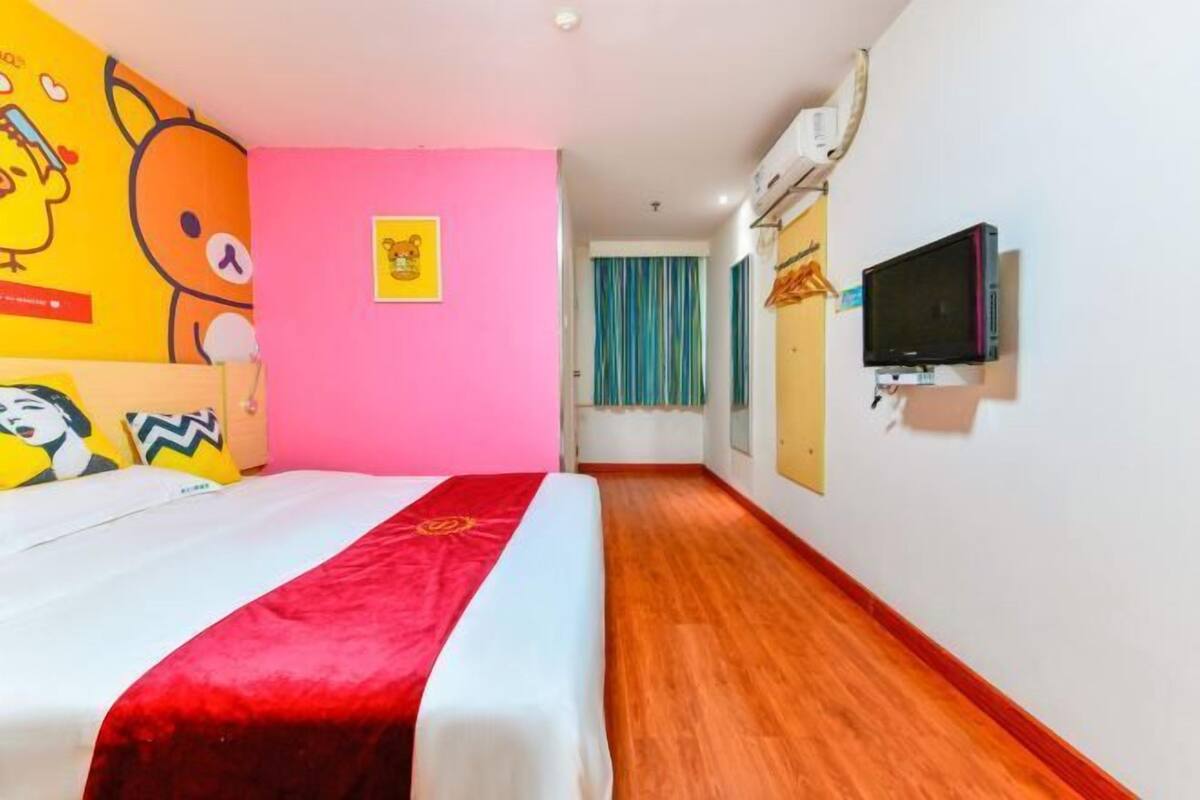 A hotel room with a bed, a television, and a pink wall.