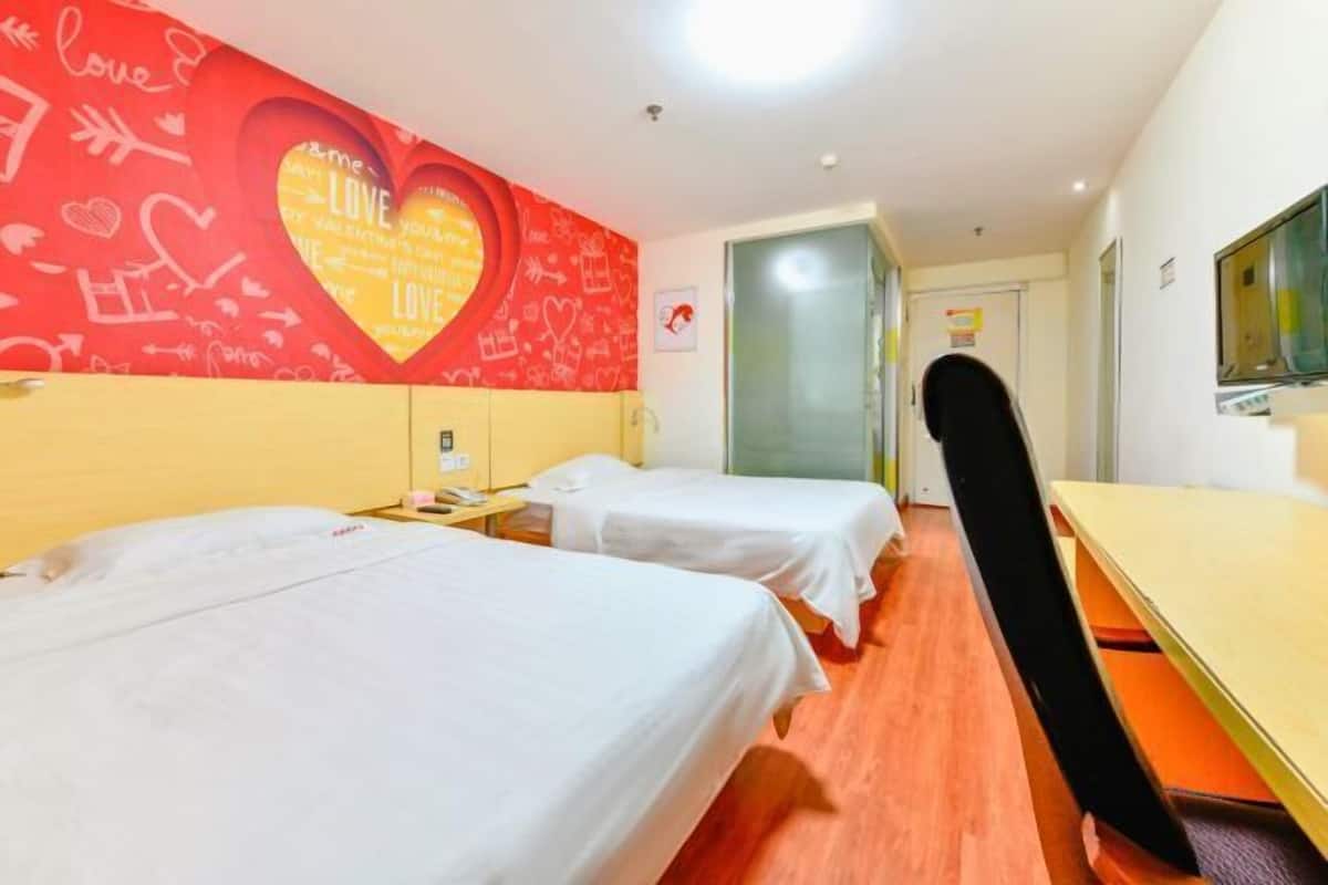 A hotel room with two beds, a desk, and a TV.