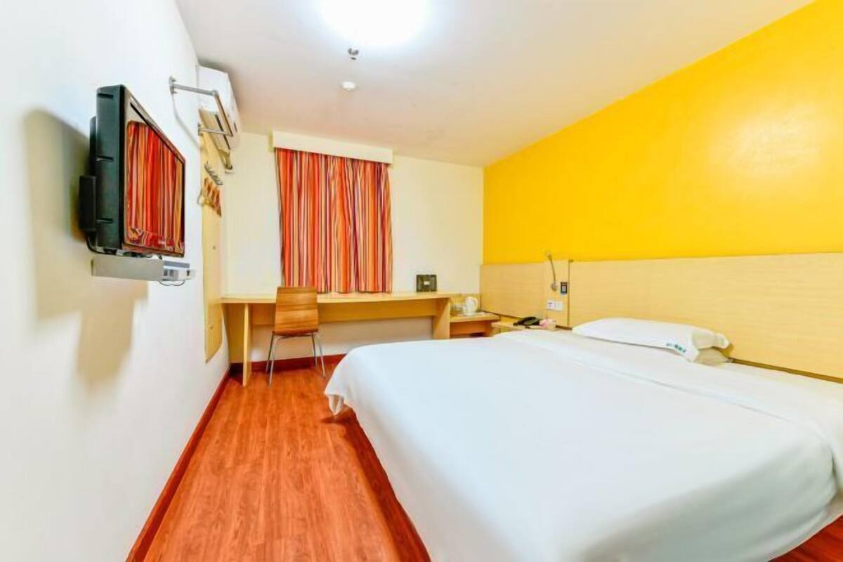 A hotel room with a bed, a desk, a chair, a TV, and a window with curtains.