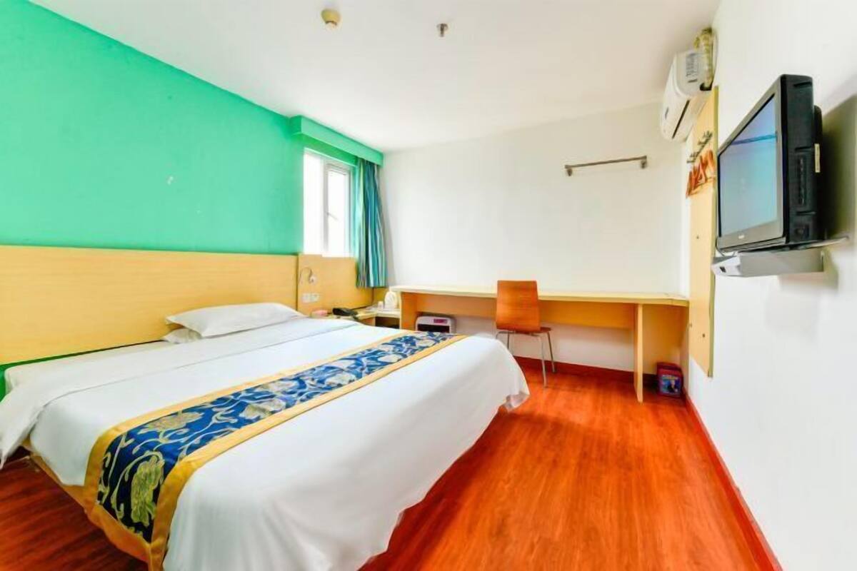 A hotel room with a bed, a desk, a chair, a television, and a window with curtains.