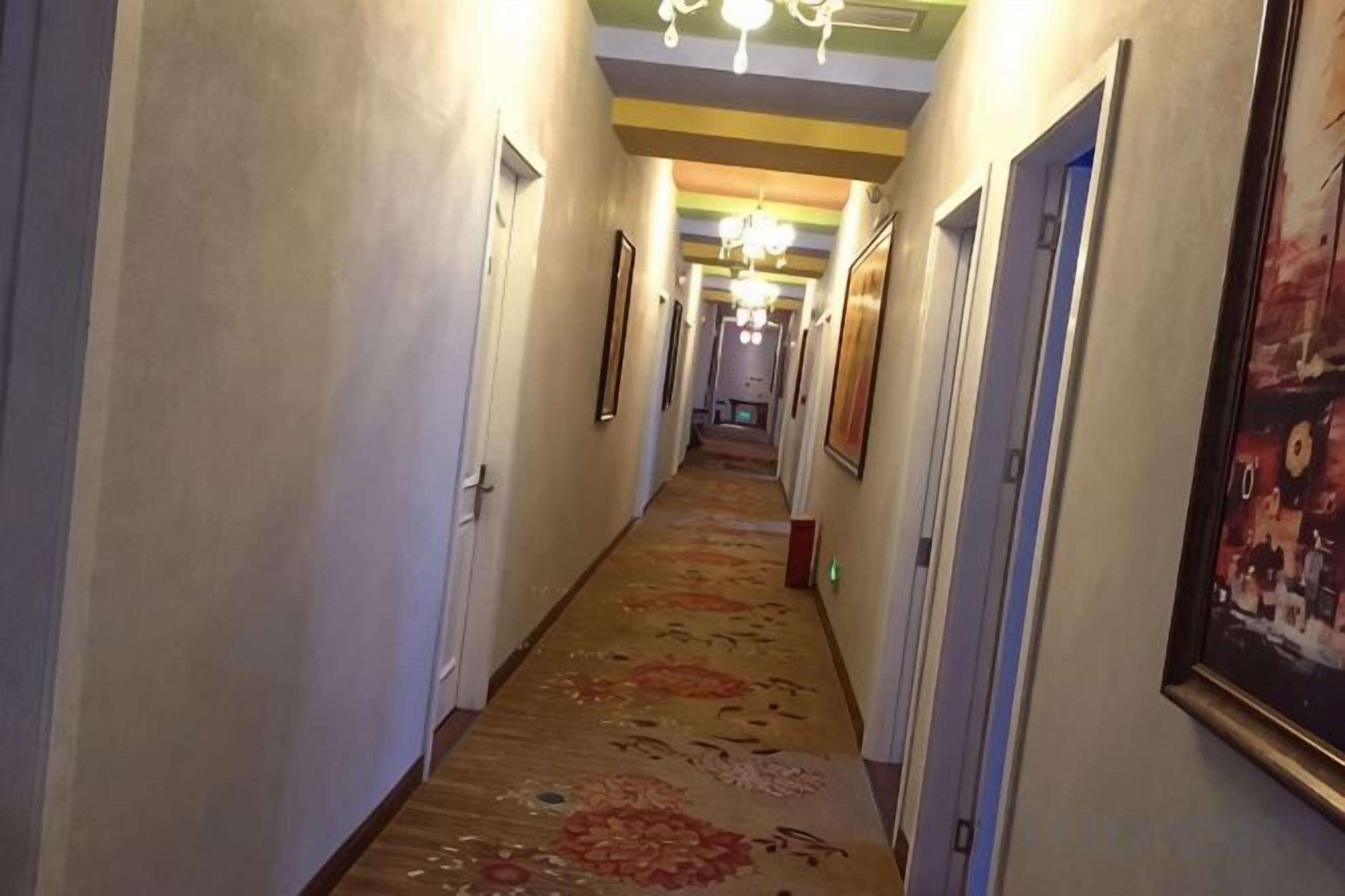 Un couloir d’hôtel avec des portes, des tableaux encadrés et une moquette à motifs.