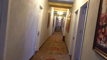 Un couloir d’hôtel avec des portes, des tableaux encadrés et une moquette à motifs.