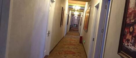 A hotel hallway with doors, framed pictures, and a patterned carpet.