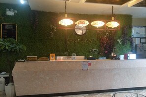 A reception desk with a green wall, a bulletin board, and a clock. - Monai Garden Hotel (Youyang County)