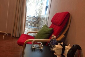 Ein Hotelzimmer mit einem roten Liegesessel, einem kleinen Tisch mit einer Wasserflasche, einer Tasse und einem Tablett.