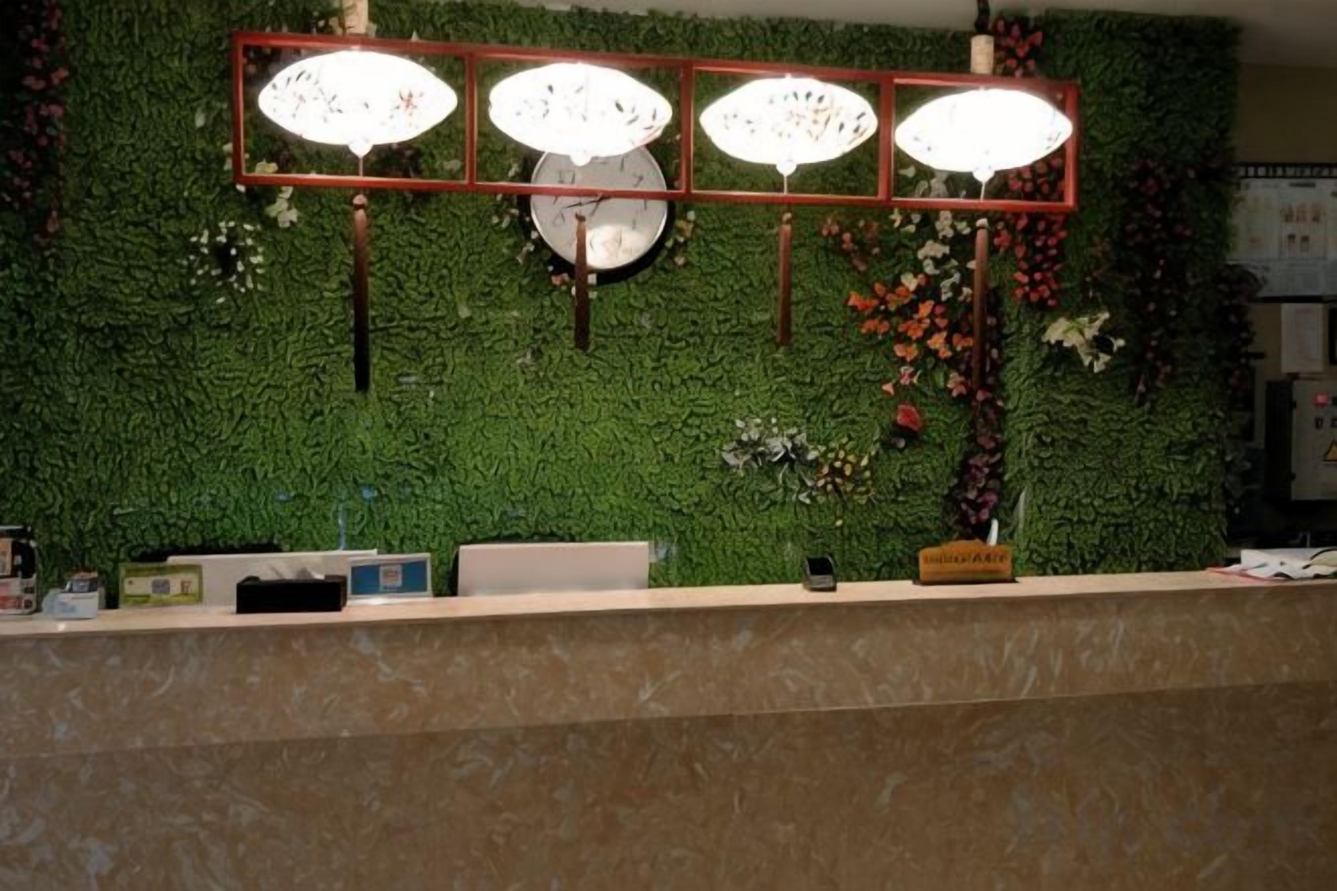 A reception desk with a green wall backdrop, a clock, and three wall-mounted lamps.
