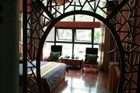 A room with a bed, two chairs, a table, and a large window.. Monai Garden Hotel