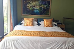 Habitación de hotel con una cama grande, dos almohadas, un cuadro en la pared y una ventana con cortinas.