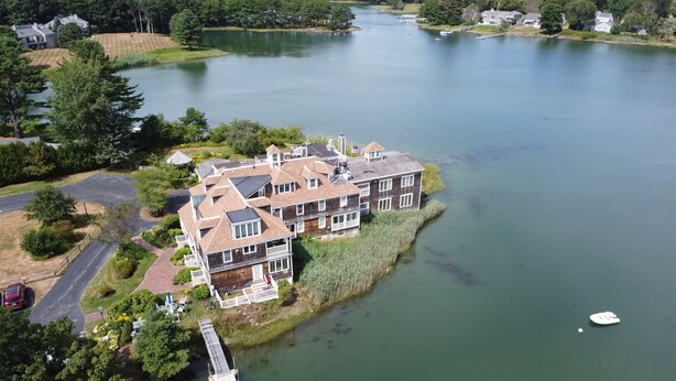 A large, multi-story house with a dock extending into a calm lake, surrounded by lush greenery. - Unique Waterfront Condo at the Boatyard! (Kennebunk)